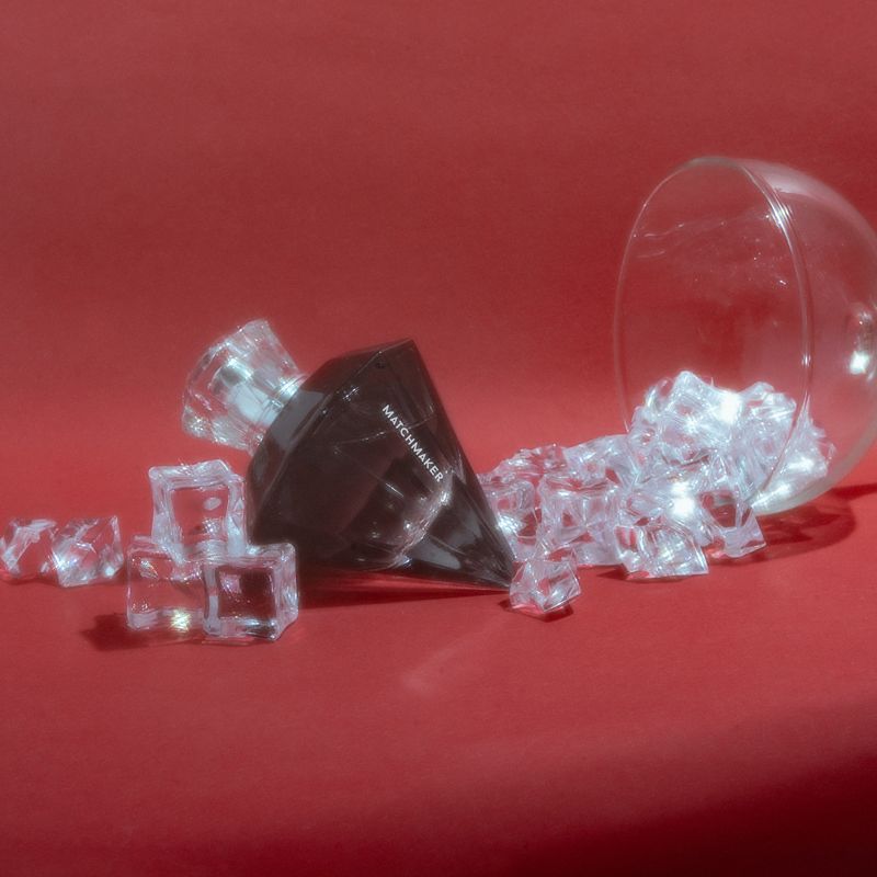 Black Diamond pheromone cologne next to a tipped cocktail glass, with crystal ice cubes appearing to spill from it.
