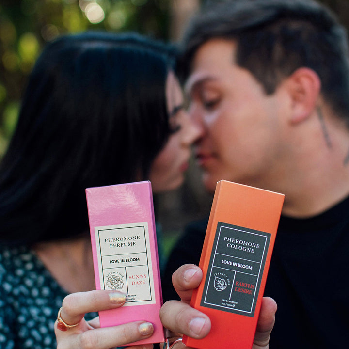 A couple in soft focus, about to kiss, holding Eye of Love's Bloom Sunny Daze pheromone perfume and Earth's Desire pheromone cologne.